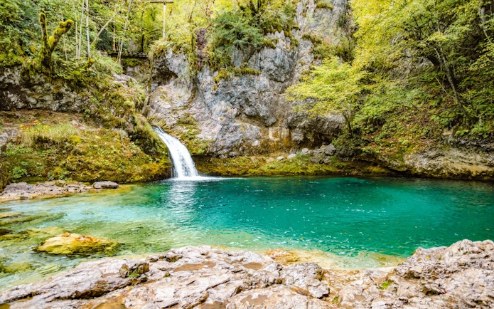 Waterfall flowing into Blue Eye spring surrounded by lush greenery in Gjirokaster.