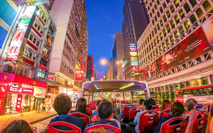 Open-top bus tour through vibrant Kowloon streets at night, Hong Kong.