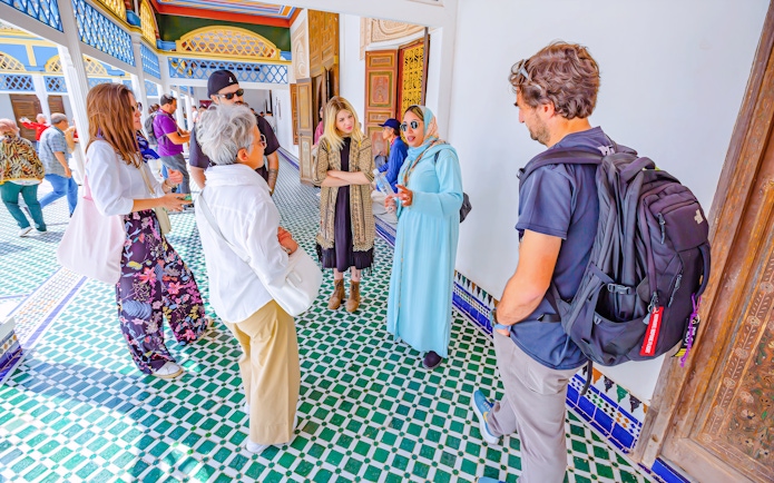 Tourists with a guide at Bahia Palace, Marrakech, Morocco, discussing architecture.