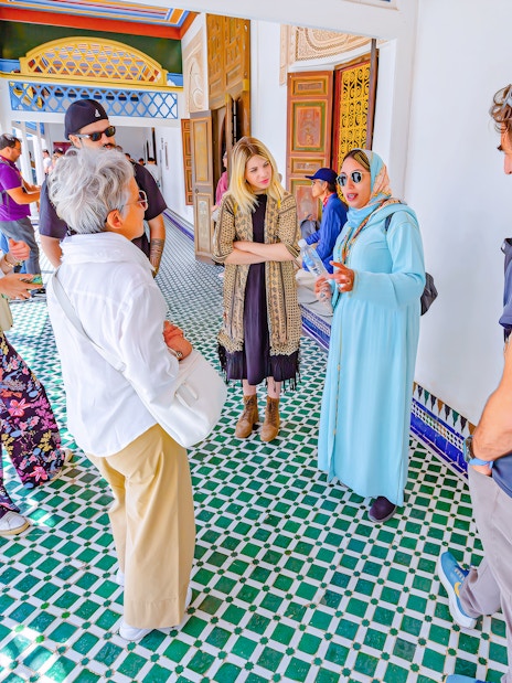 Tourists with a guide at Bahia Palace, Marrakech, Morocco, discussing architecture.
