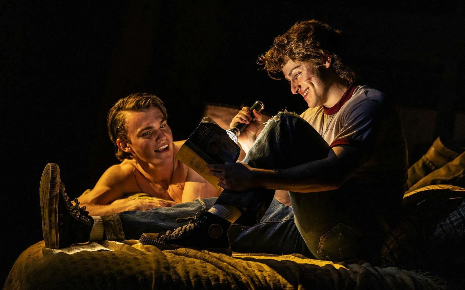 Two actors reading a book with a flashlight during The Outsiders stage performance on Broadway.