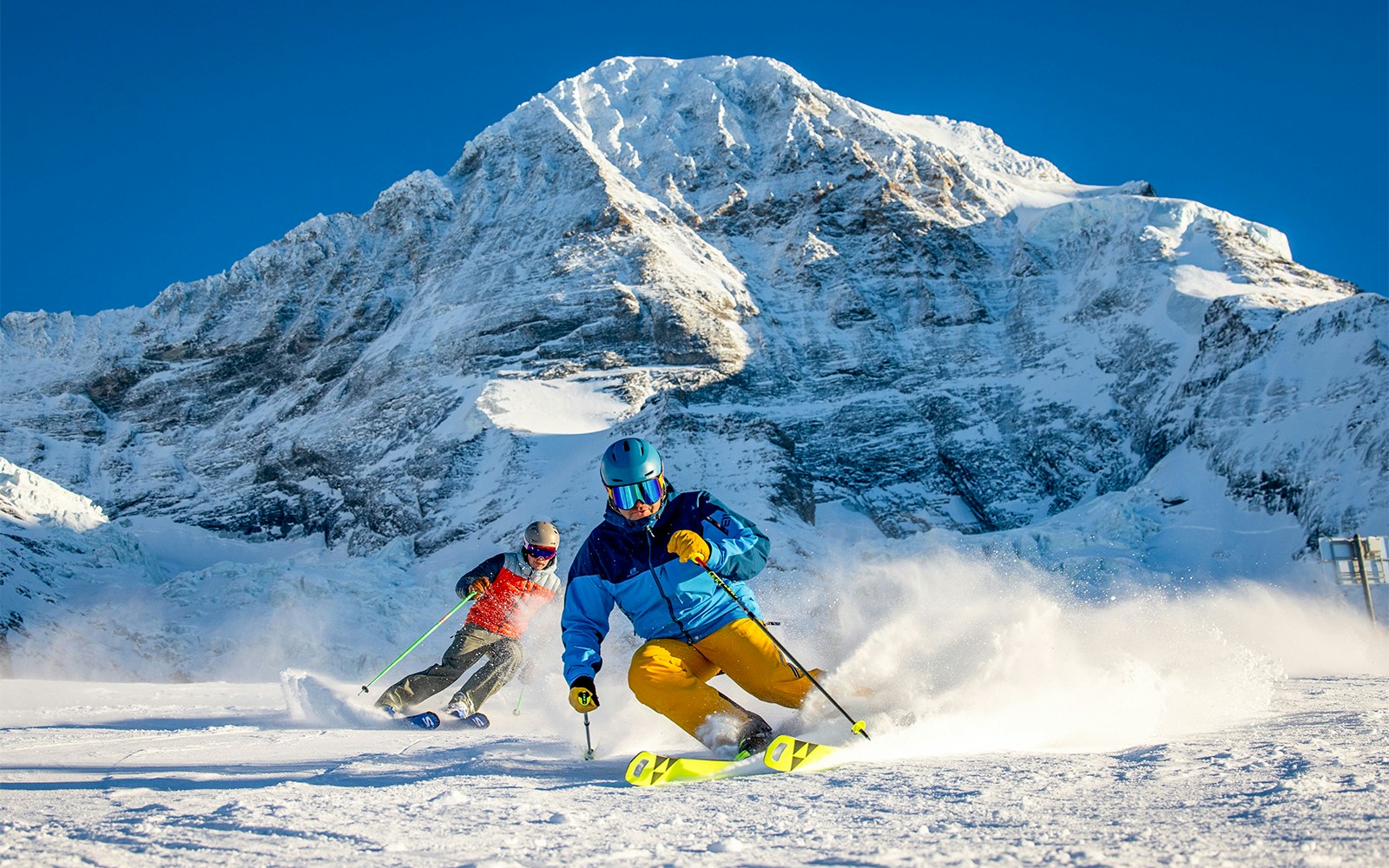 Skiers enjoying slopes at Bodmi Arena, Grindelwald First, with snow-covered mountains in the background.