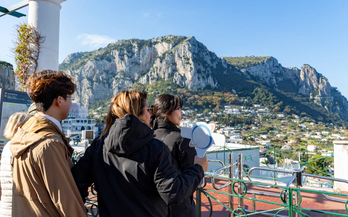 Tour guide with tourists overlooking Capri landscape near the dock.