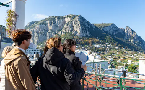Tour guide with tourists overlooking Capri landscape near the dock.