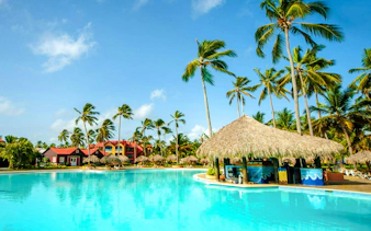 Large outdoor swimming pool with thatched-roof pool bar at Punta Cana Princess.