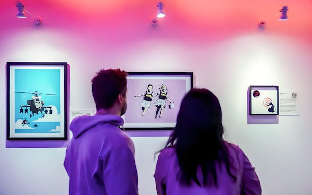 Visitors viewing Banksy artwork at an exhibition, featuring iconic pieces.