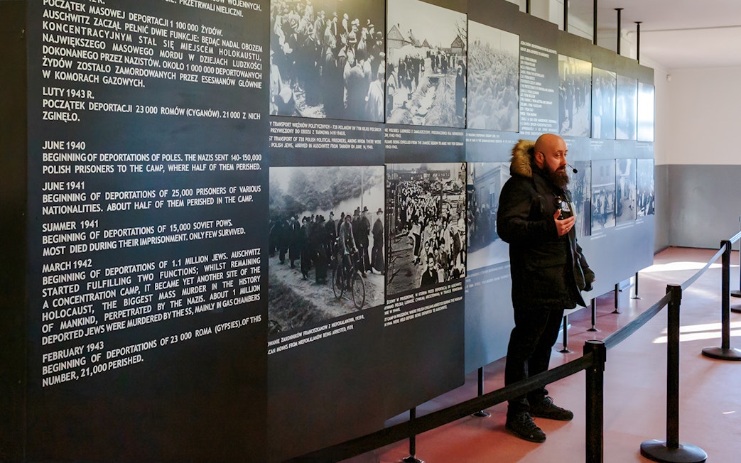 Guide explaining historical exhibits at Auschwitz Birkenau to visitors.