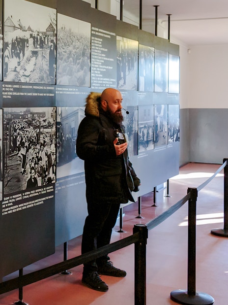 Guide explaining historical exhibits at Auschwitz Birkenau to visitors.