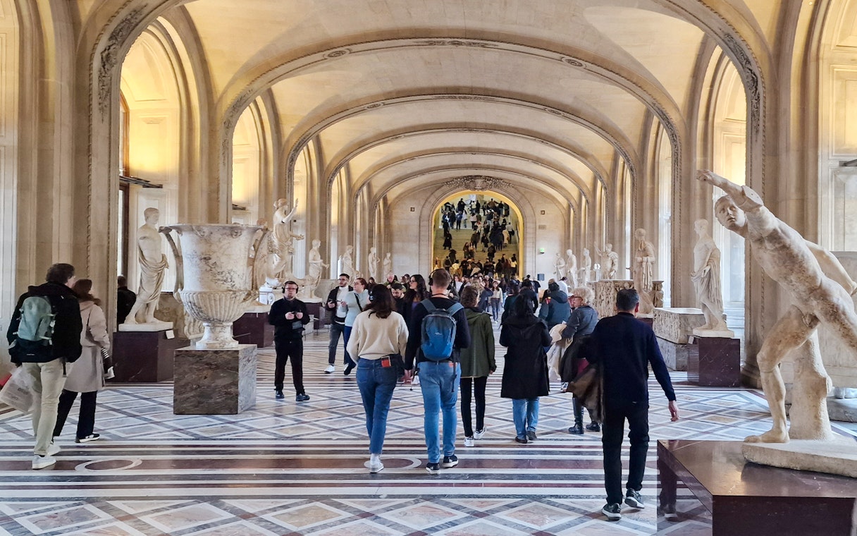 Tourists walking through a sculpture gallery at the Louvre Museum in Paris, France.