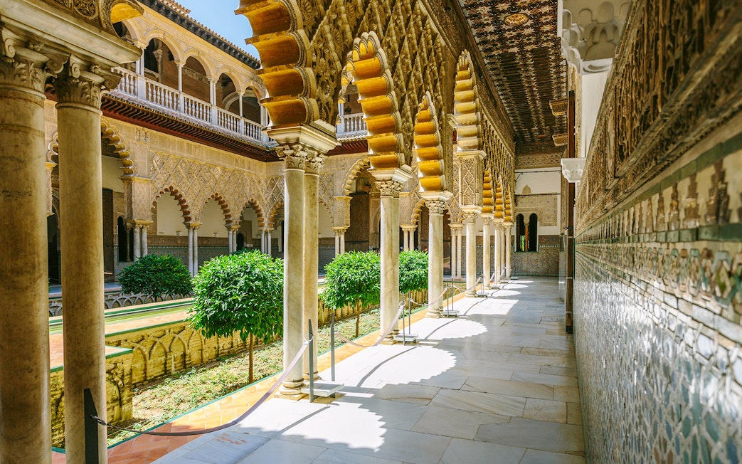Alcazar of Seville courtyard with ornate arches and lush greenery.