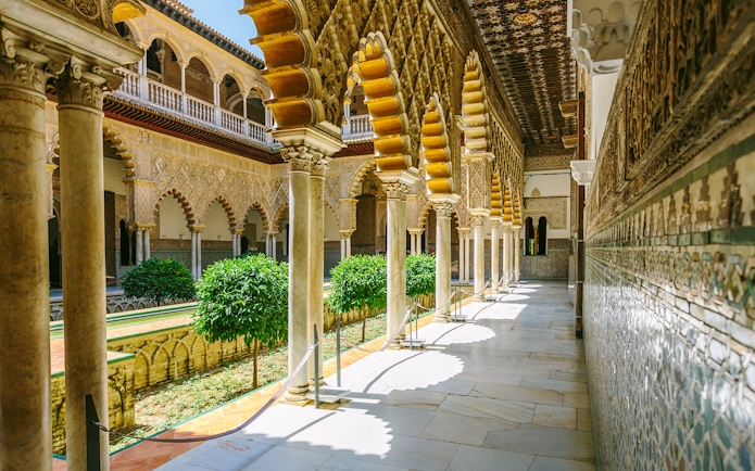 Alcazar of Seville courtyard with ornate arches and lush greenery.