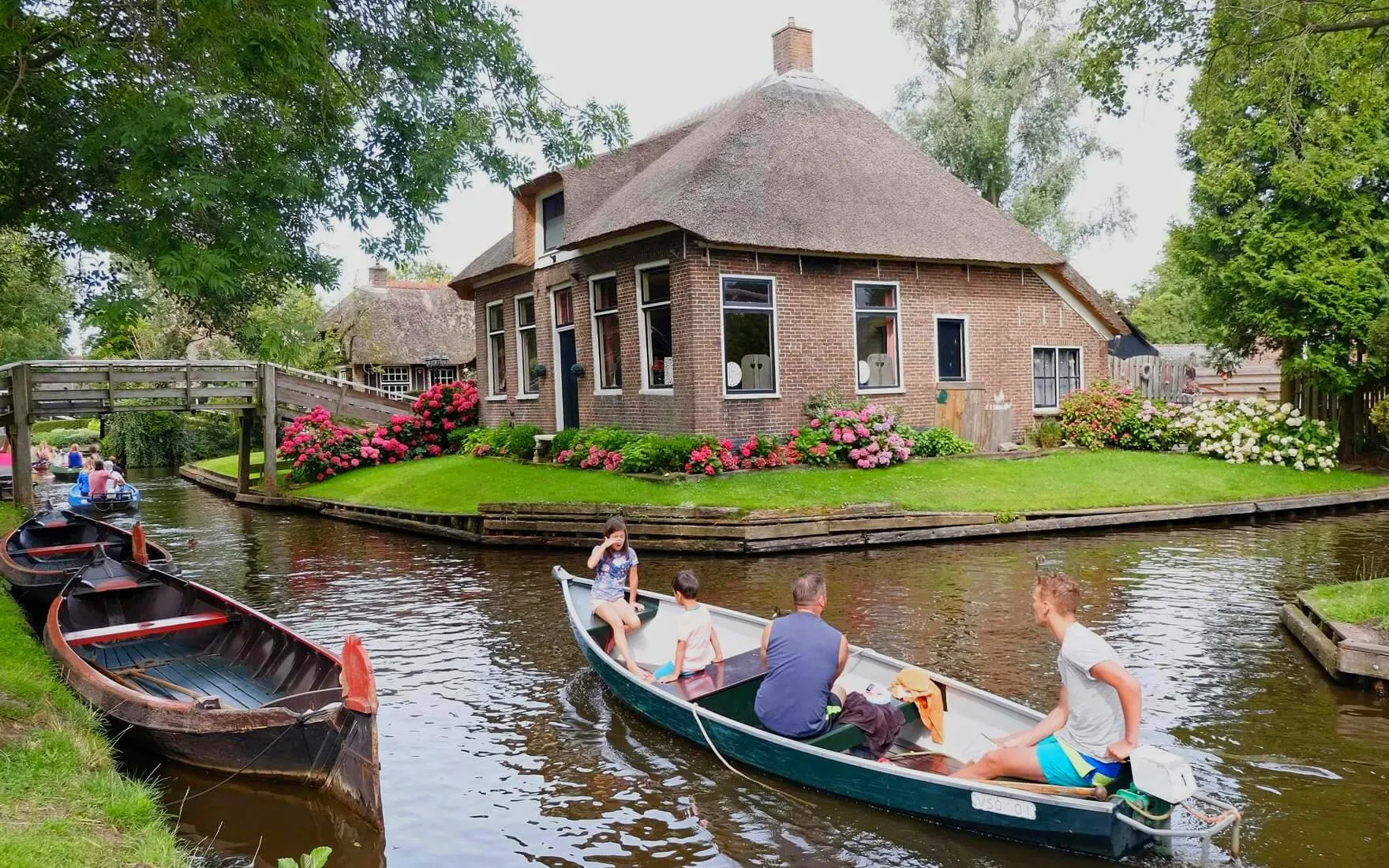 Boat tour on a canal in Giethoorn, passing a traditional thatched-roof house and wooden bridge.