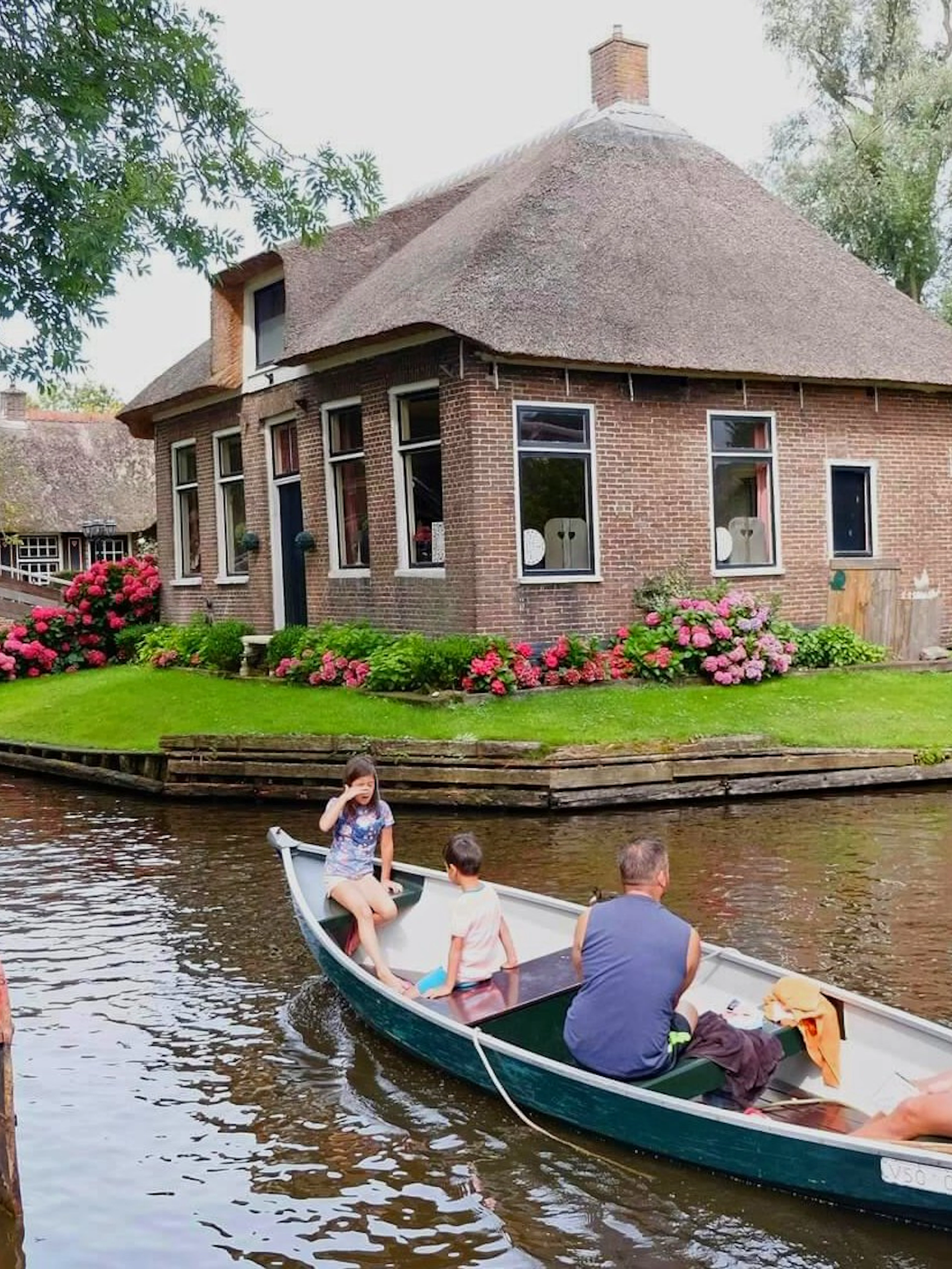 Boat tour on a canal in Giethoorn, passing a traditional thatched-roof house and wooden bridge.