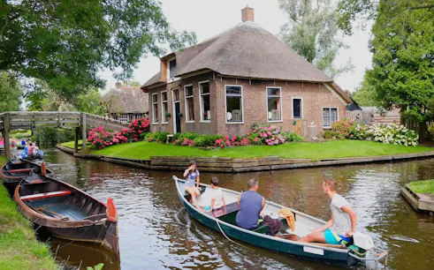 Boat tour on a canal in Giethoorn, passing a traditional thatched-roof house and wooden bridge.