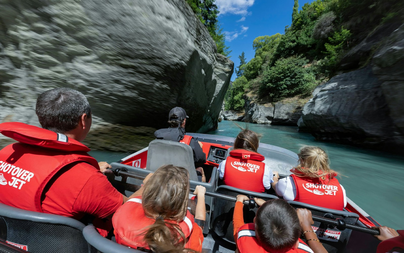 Shotover Jet with tourists in lifejackets navigating narrow canyon in New Zealand.