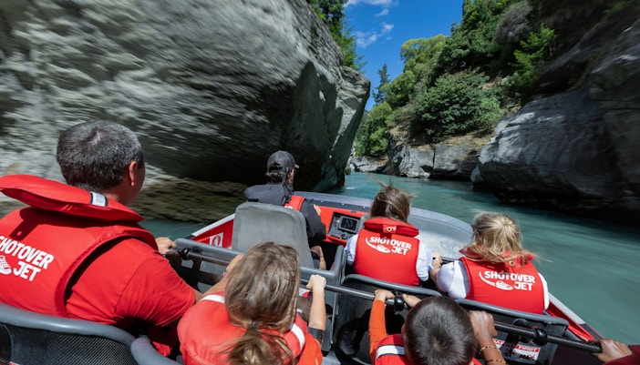 Shotover Jet with tourists in lifejackets navigating narrow canyon in New Zealand.