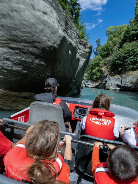 Shotover Jet with tourists in lifejackets navigating narrow canyon in New Zealand.