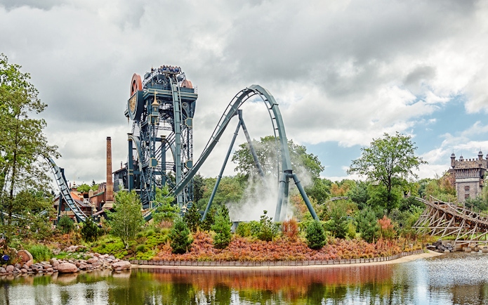 Dive coaster The Baron at Efteling amusement park, Netherlands, with riders and scenic surroundings.