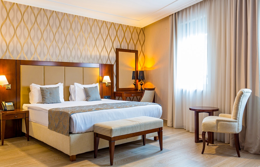 Mid-range hotel room with bed, desk, and window view in a city setting.