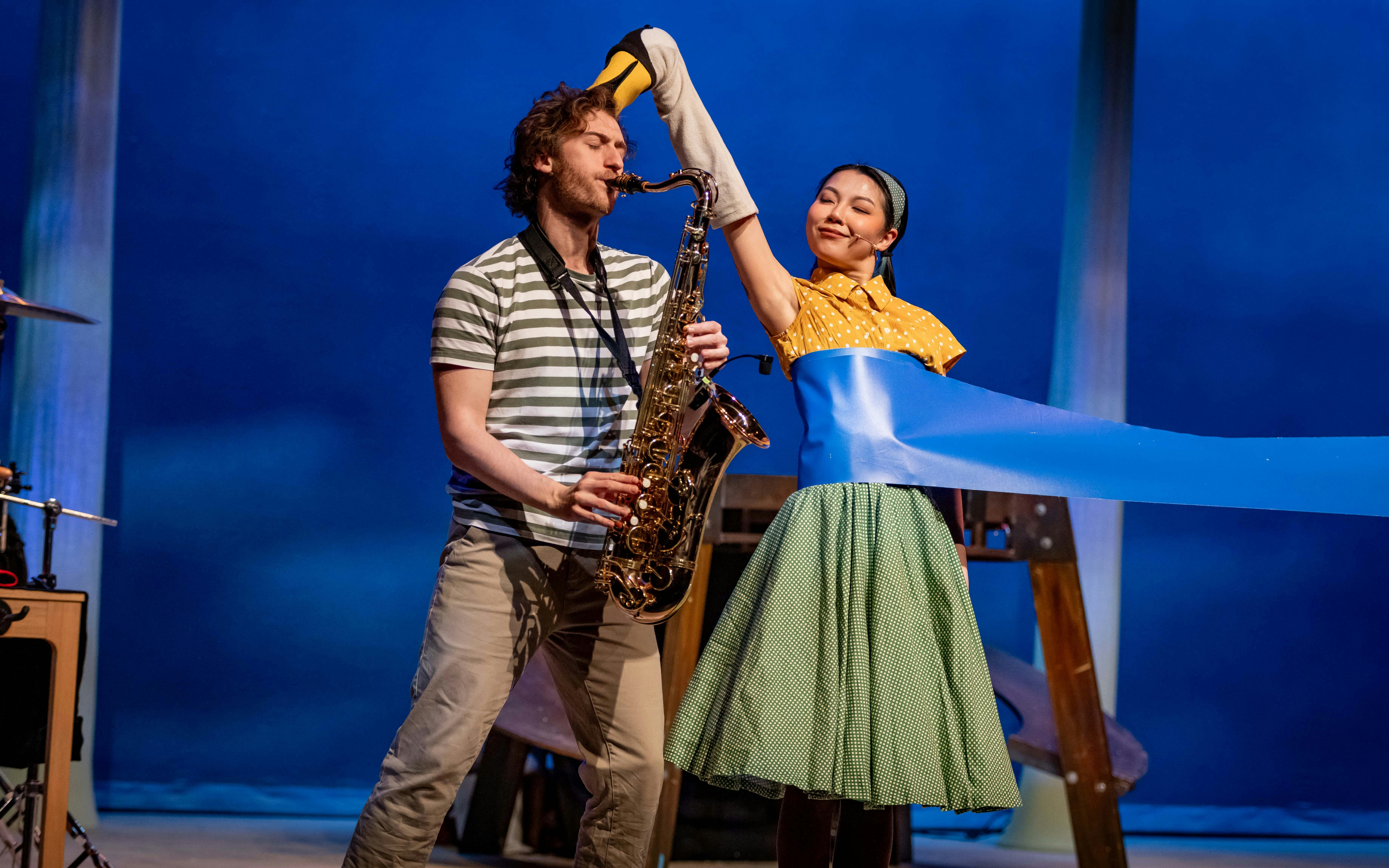 Stage performance of Stick Man in Westend with saxophonist and performer holding puppet.