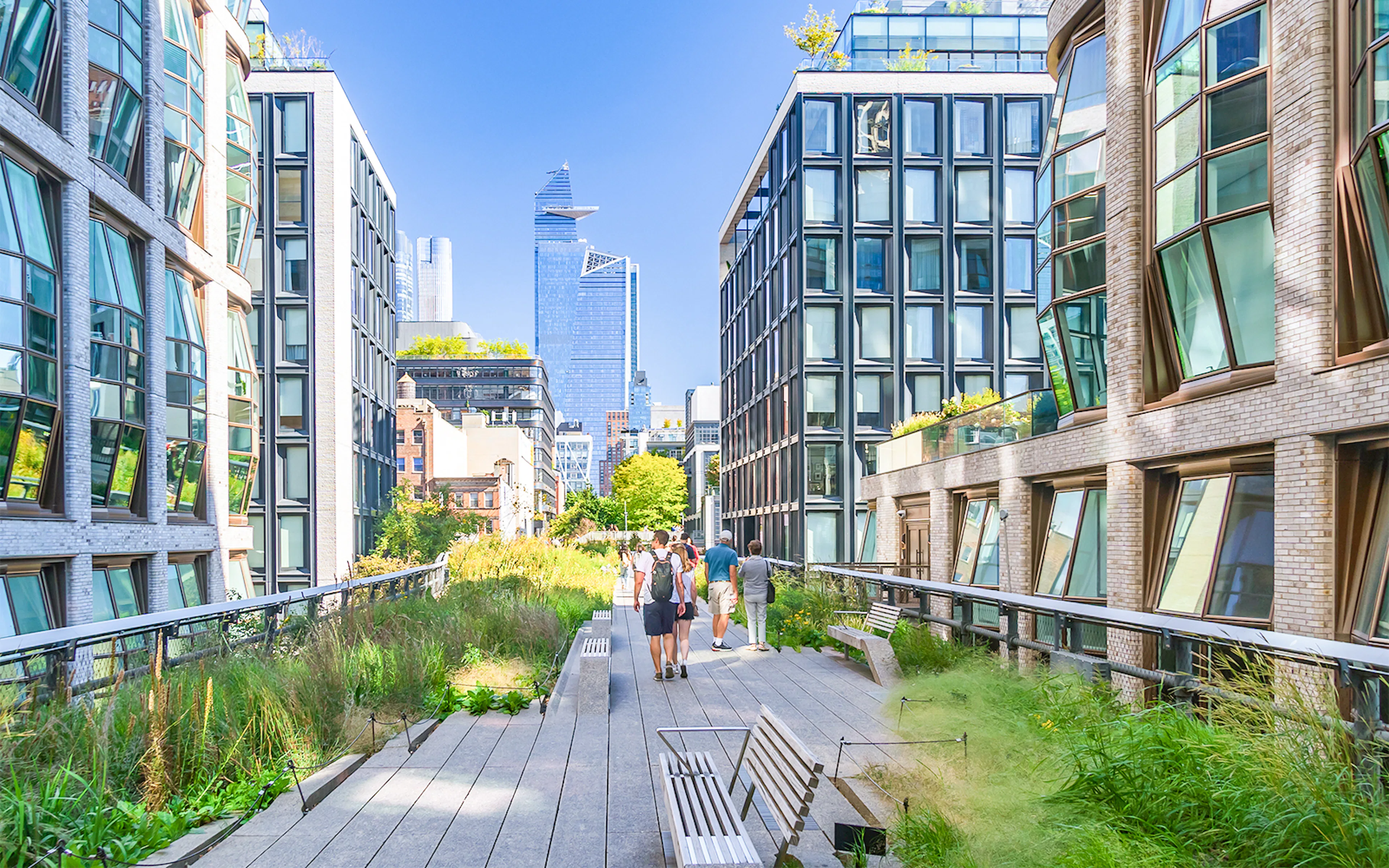 People walking on The High Line, a public park in Manhattan, New York, with city buildings in view.