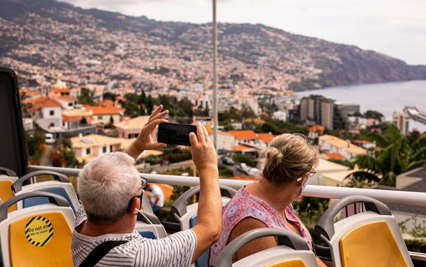 Tourists on a Funchal bus tour capturing city views with mountains and ocean in the background.