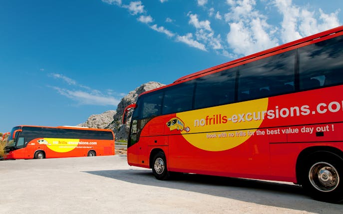 Red tour buses parked with rocky landscape in Mallorca, part of sightseeing tour with boat and vintage train.