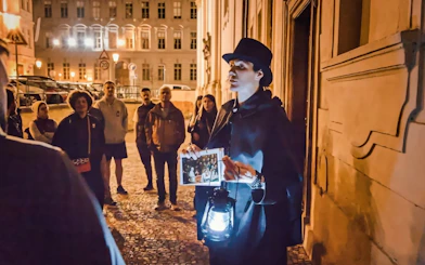 Guide leading Ghosts & Legends tour in Old Town Prague at night with lantern.