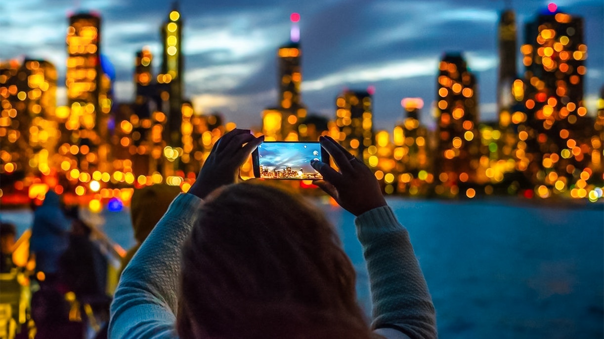 Person photographing Chicago skyline during Lake Michigan sunset cruise.