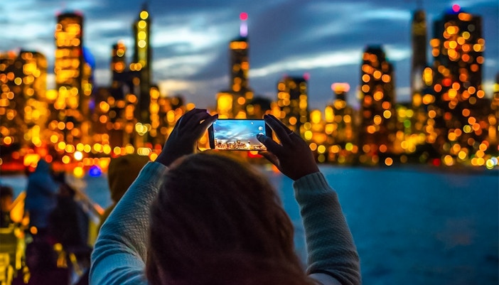 Person photographing Chicago skyline during Lake Michigan sunset cruise.