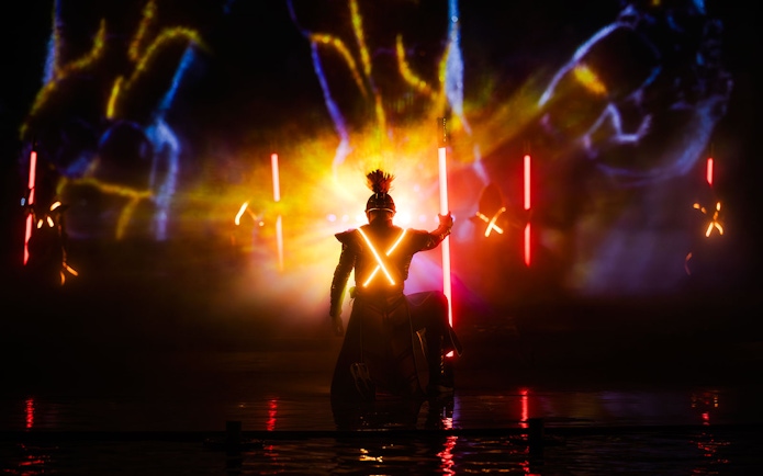 Performer in illuminated costume during Kiss of the Sea Show with vibrant lights.
