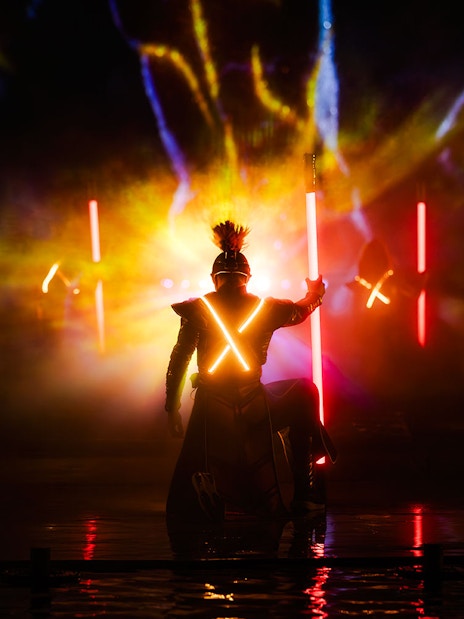 Performer in illuminated costume during Kiss of the Sea Show with vibrant lights.
