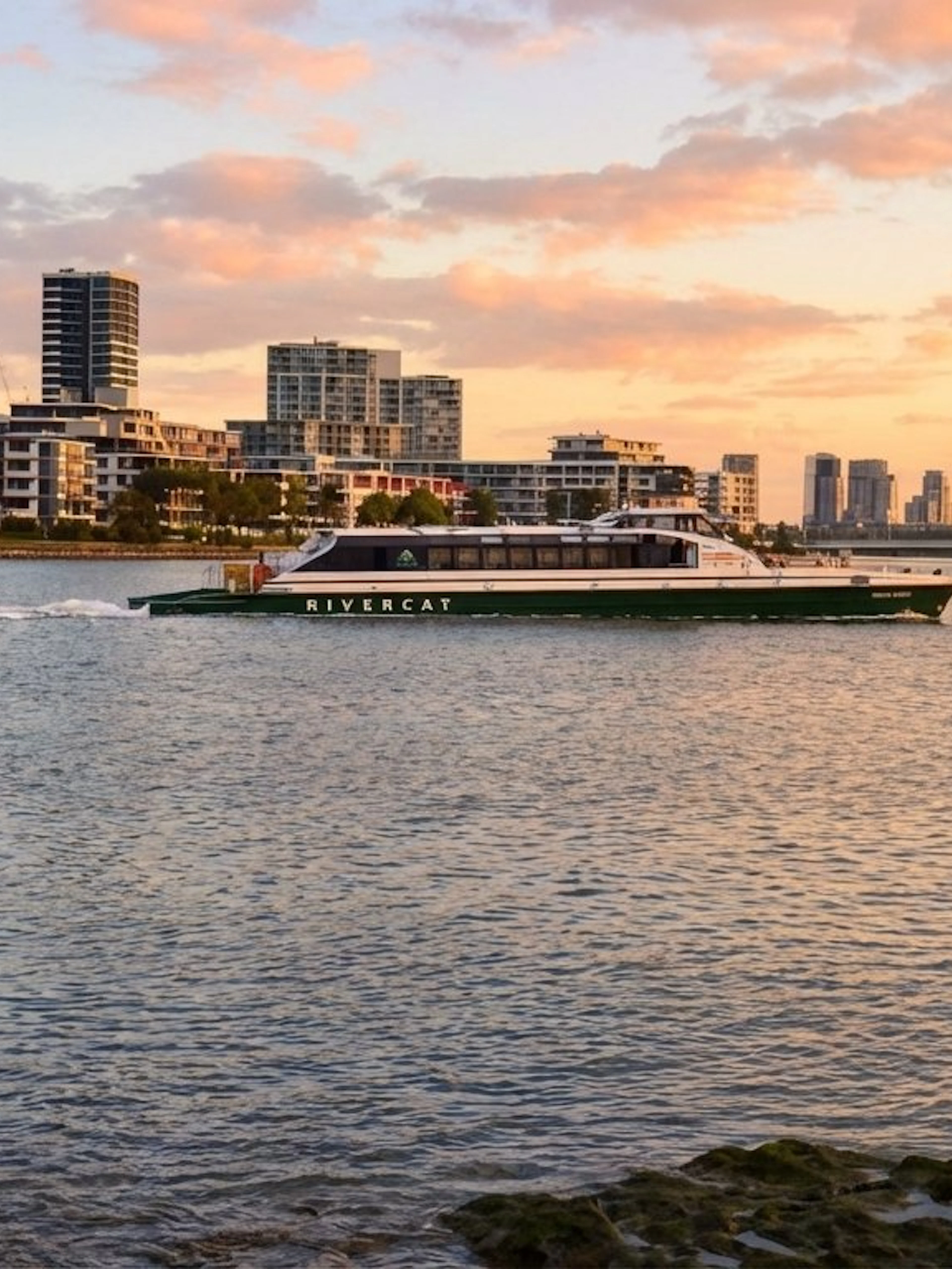 River cat ferry on Parramatta River in Sydney at sunset with city skyline.