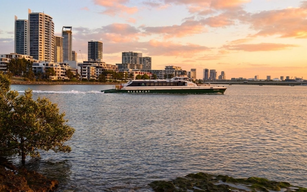 River cat ferry on Parramatta River in Sydney at sunset with city skyline.