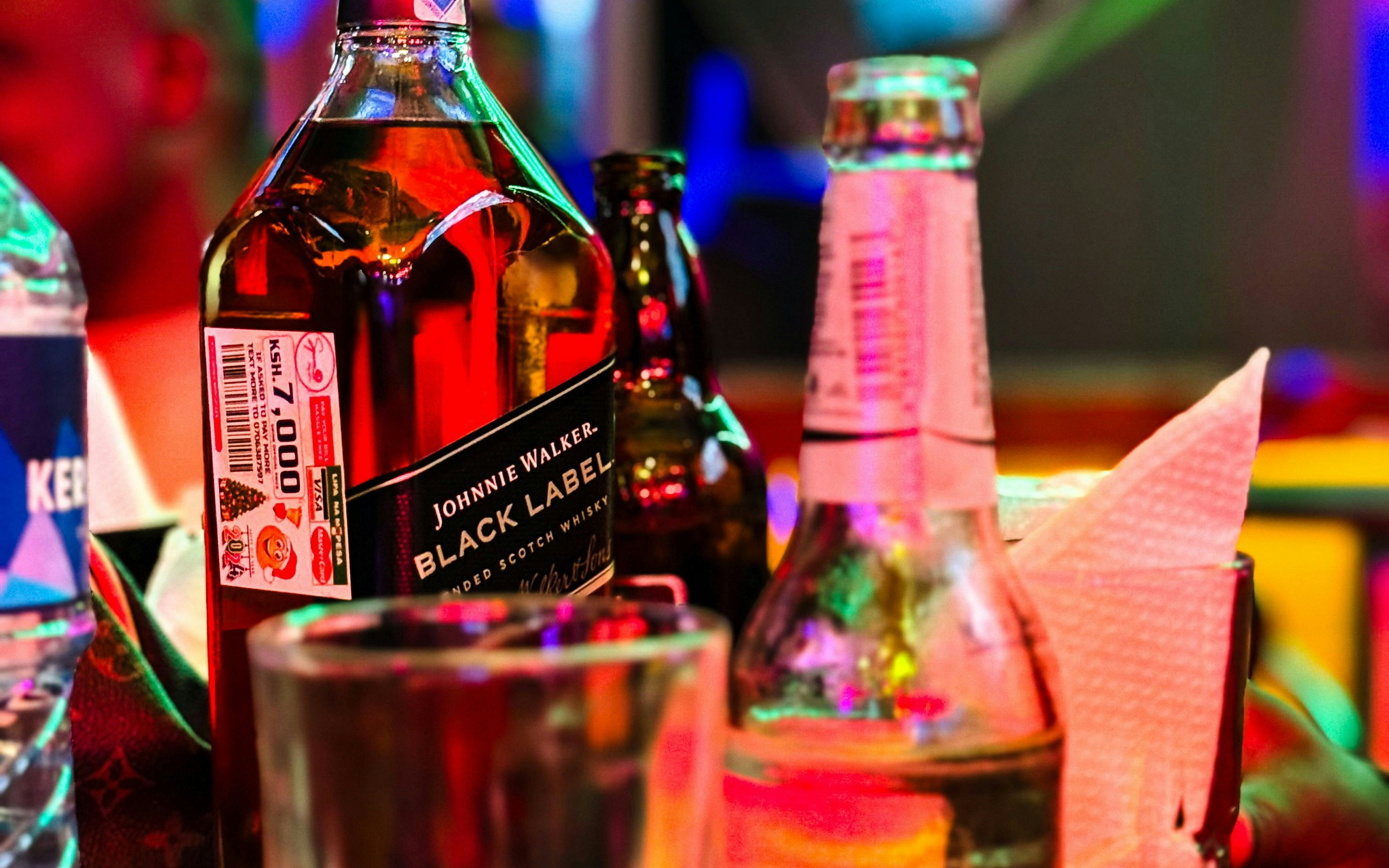 Johnnie Walker Black Label bottle on a colorful bar table with drinks.