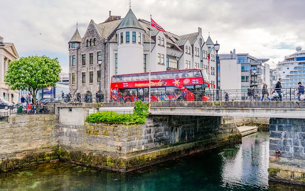 Alesund hop-on hop-off bus crossing a bridge near historic buildings in Norway.