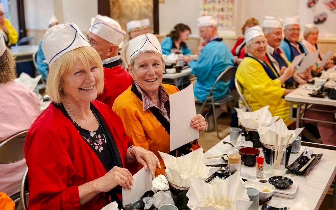 Tourists enjoying a sushi-making workshop in Osaka, wearing traditional attire.
