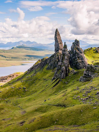 Old Man of Storr rock formation on the Isle of Skye, Scotland, with rolling green hills.