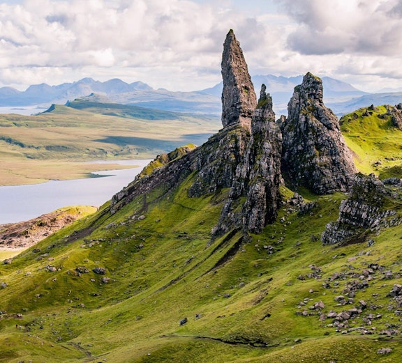 Old Man of Storr rock formation on the Isle of Skye, Scotland, with rolling green hills.