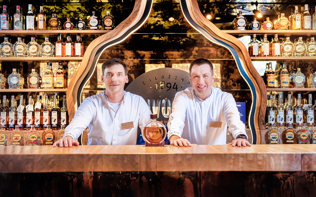 Slivovitz Museum staff at tasting bar with plum brandy bottles in background.