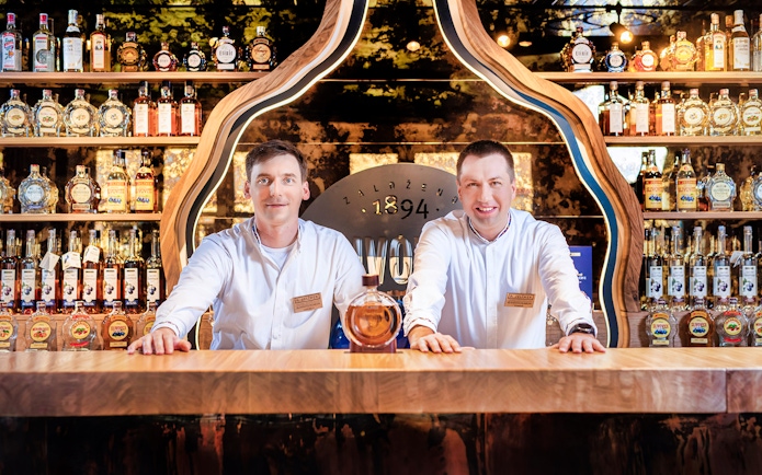 Slivovitz Museum staff at tasting bar with plum brandy bottles in background.