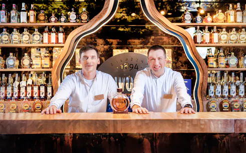 Slivovitz Museum staff at tasting bar with plum brandy bottles in background.