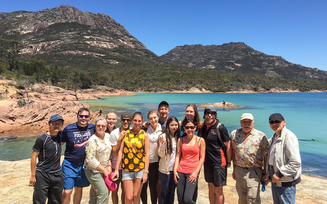 Group of tourists at Wineglass Bay with mountains and turquoise water in the background, Tasmania.