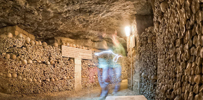 Ghostly figure in Paris Catacombs corridor with skull-lined walls.