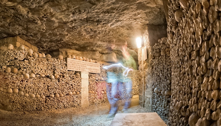 Ghostly figure in Paris Catacombs corridor with skull-lined walls.
