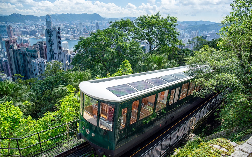 Peak Tram ascending through lush greenery with Hong Kong skyline in the background.