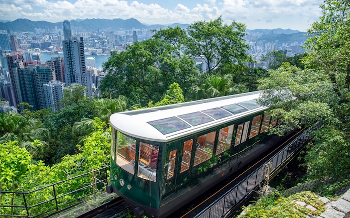 Peak Tram ascending through lush greenery with Hong Kong skyline in the background.