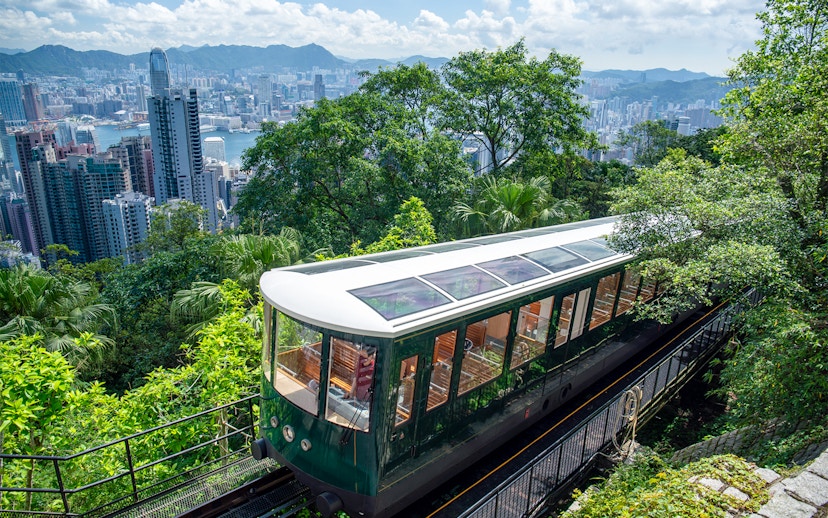 Peak Tram ascending through lush greenery with Hong Kong skyline in the background.