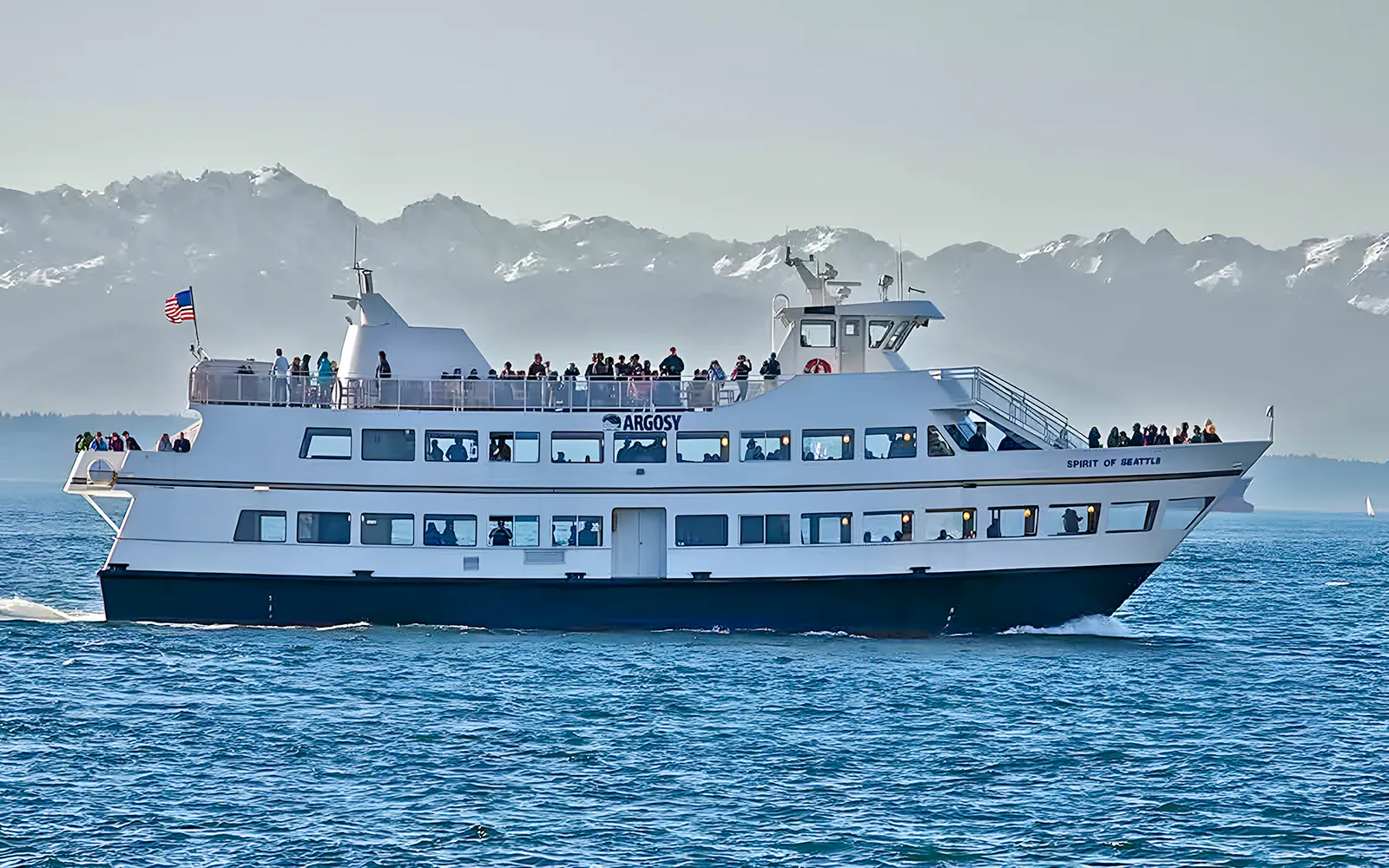 Ferry "Spirit of Seattle" cruising with passengers, mountains in background, Seattle CityPASS® tour.