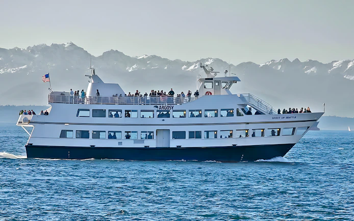 Ferry "Spirit of Seattle" cruising with passengers, mountains in background, Seattle CityPASS® tour.